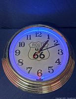 Front view of Route US 66 neon clock illuminated with blue neon light, showing Route 66 shield logo and clear numbering.