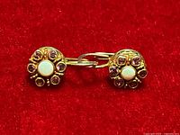 Front view of the pair of gold plated sterling silver earrings featuring central opal stones surrounded by pink tourmalines on red velvet background.