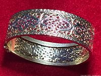 Close-up image showing ornate filigree and diamond cut design on sterling silver gold plated bracelet against red background.