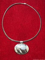 Full view of the sterling silver omega torque necklace with oval abalone shell pendant against a red background.