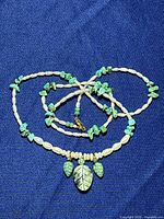 Turquoise and pearl necklace laid flat on dark blue fabric, showing detailed carved leaf pendants and pearl beads.