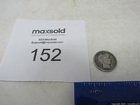 Top-down view of 1914 Barber Dime coin next to a MaxSold lot number card and ruler for scale.