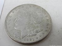 Close-up photo of the obverse side of the 1921 silver dollar coin showing the profile of Lady Liberty and date 1921 with surrounding inscriptions.
