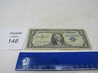 Front view of the 1957 A Blue Seal Silver Certificate $1 bill with ruler for scale and lot number card.