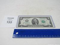 Front view of $2 bill in sleeve with identification tag and ruler