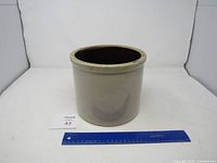 Photo of antique stoneware crock with scale for size reference, showing a beige crock with a darker glazed interior and some minor surface markings.
