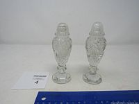 Pair of clear crystal salt and pepper shakers with intricate faceted cut design, displayed with a ruler for size reference on flat surface.