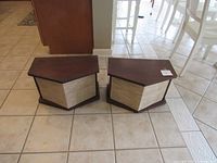 Pair of trapezoidal wood veneer speakers with beige cloth fronts on tiled floor