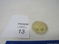 Gold coin replica next to MaxSold lot number card for scale and identification.