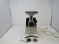 Front view of Hamilton Beach electric meat grinder with power cord and two grinding plates in front on white surface.