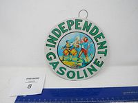 Front view of the metal round sign with Independent Gasoline text and colonial-era drum players illustration.