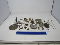 Overview of assorted small metal collectibles including plates, figurines, skewers, bell, miniature car, and knives arranged on white background.