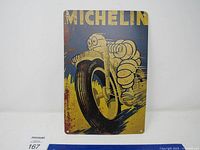 Front view of the rectangular metal sign showing Michelin Man riding a motorcycle tire with blue and yellow colors and some rust spots and wear.