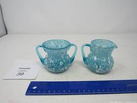 Blue glass creamer and sugar bowl with white spots shown side by side with a ruler for size reference.