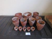 Collection of various sizes of clay garden pots arranged in groups on a wooden surface with a white label showing lot 109.