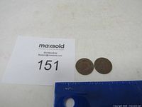 Two Indian Head pennies placed side by side with ruler for scale and lot number visible.