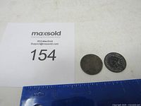 Photo showing two Indian Head pennies next to a blue ruler and MaxSold lot number card