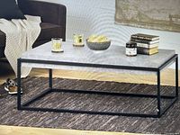 Coffee table in a living room setting showing rectangular stone-look top and black metal frame
