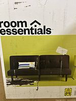 Image showing the Room Essentials branding and the black sofa with a decorative pillow and minimalist styling on the packaging box.