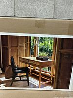Photo of the boxed Threshold Minsmere Writing Desk showing the assembled desk in a wood-paneled room with a black chair and decor items on top.