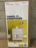 Photo of the box showing the product brand 'room essentials' and front view image of the dresser with four drawers against a yellow backdrop.