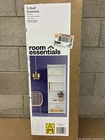 Photo of the cardboard box packaging, showing the brand 'room essentials' and bookcase image.