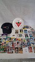 Full layout showing assortment of baseball and basketball cards spread out, Canadian Tire frisbee and New England Patriots baseball cap placed centrally