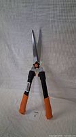 Front view of Fiskars manual hedge shears showing orange and black handles with long sharp blades