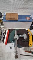 Photo of cork sanding block, utility knives, Delta tool, and a sanding belt box on a black circular surface