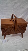 Closed view showing hardwood sewing box with handle, four legs, and folding arm mechanism.