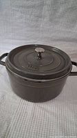 Gray cast-iron pot with lid, showing Staub embossed logo on the lid and two handles on either side.