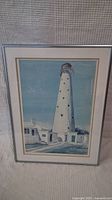 Framed lighthouse print showing full artwork and framing with light blue sky and lighthouse.