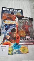 Photo showing Marvel Legends Spawn of Symbiotes figure in packaging alongside three magazines: two Den of Geek and one Superman magazine.