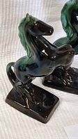 Close-up of one black ceramic prancing horse figurine with blue-green glaze accents and rectangular base.