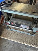 Full front view of the thickness planer on a workshop floor, showing frame, tables and hose attachment.