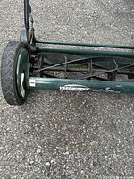 Close-up of the left wheel and cutting reel of a green Yardworks lawn mower with 18 inch cutting width decal.