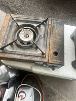 Photo shows Coleman butane portable burner stove, metal rectangular body, rust spots on surface, single burner with four prongs