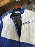 Close-up of upper part of blue and white Fast Lane kart racing suit showing logo and zipper.
