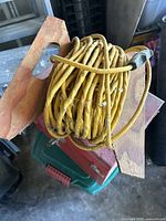 Yellow extension cord coiled on a wooden holder with hand slots, showing signs of wear and dirt.