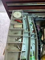 Top view of compartmentalized tackle box showing metal wrench, orange cutter, spools and fishing lures