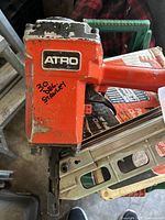 Orange ATRO framing nailer with hand-written notes on the side and visible wear.