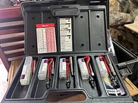 Opened Helicoil thread repair kit showing multiple sizes of inserts and installation tools inside plastic case compartments.