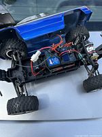 RC mini monster truck with blue body showing wiring and chassis on a reflective surface
