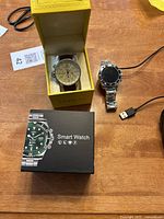Invicta left-handed watch in yellow box, smart watch with stainless steel band and charging cable on table with original smart watch box