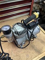 Small 110 V low pressure air compressor with pressure gauge and filter bowl, showing fabric wrapped handle and power cord.