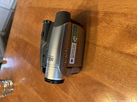Photo of silver Sony Handycam camcorder with lens closed, showing Sony branding and Carl Zeiss Vario-Tessar lens information.