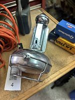 Close-up of chrome trouble light with protective cage and coiled orange power cord among other vintage lights on a wooden surface