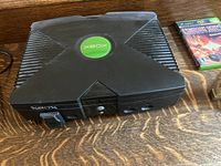 Photo showing original black Xbox console with green logo on top and front load DVD drive