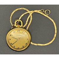 Front view of gold-tone Caravelle pocket watch with flat patterned chain, showing dial