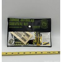 Front view of sealed Zombie Outbreak Survival Kit pouch with measuring tape for scale